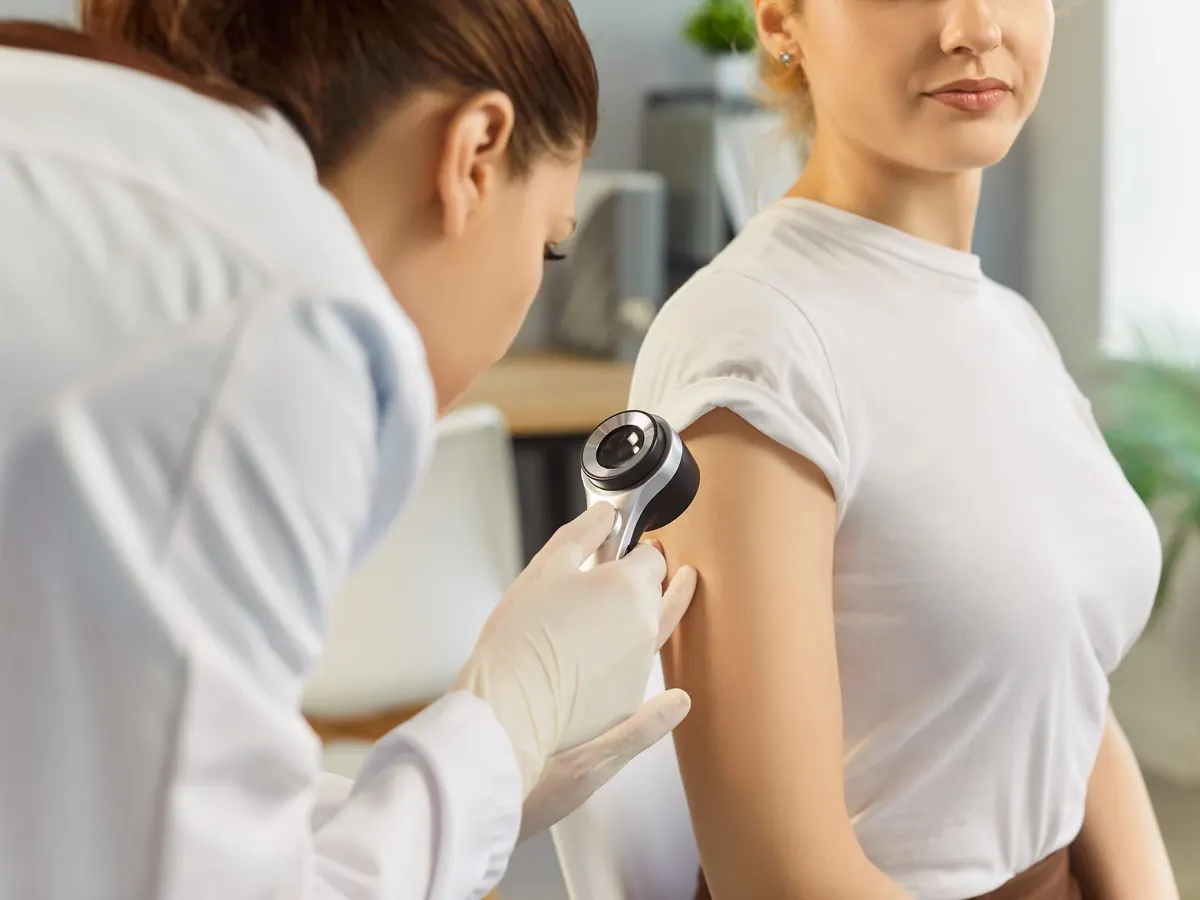 Stock photograph of models: a dermatologist in gloves examines a young woman’s upper arm with a dermatoscope