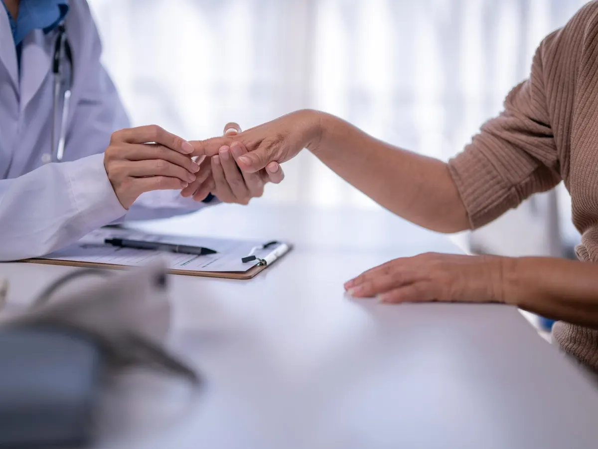 Stock photograph of models: a doctor in a white coat examines a patient’s hand across a desk