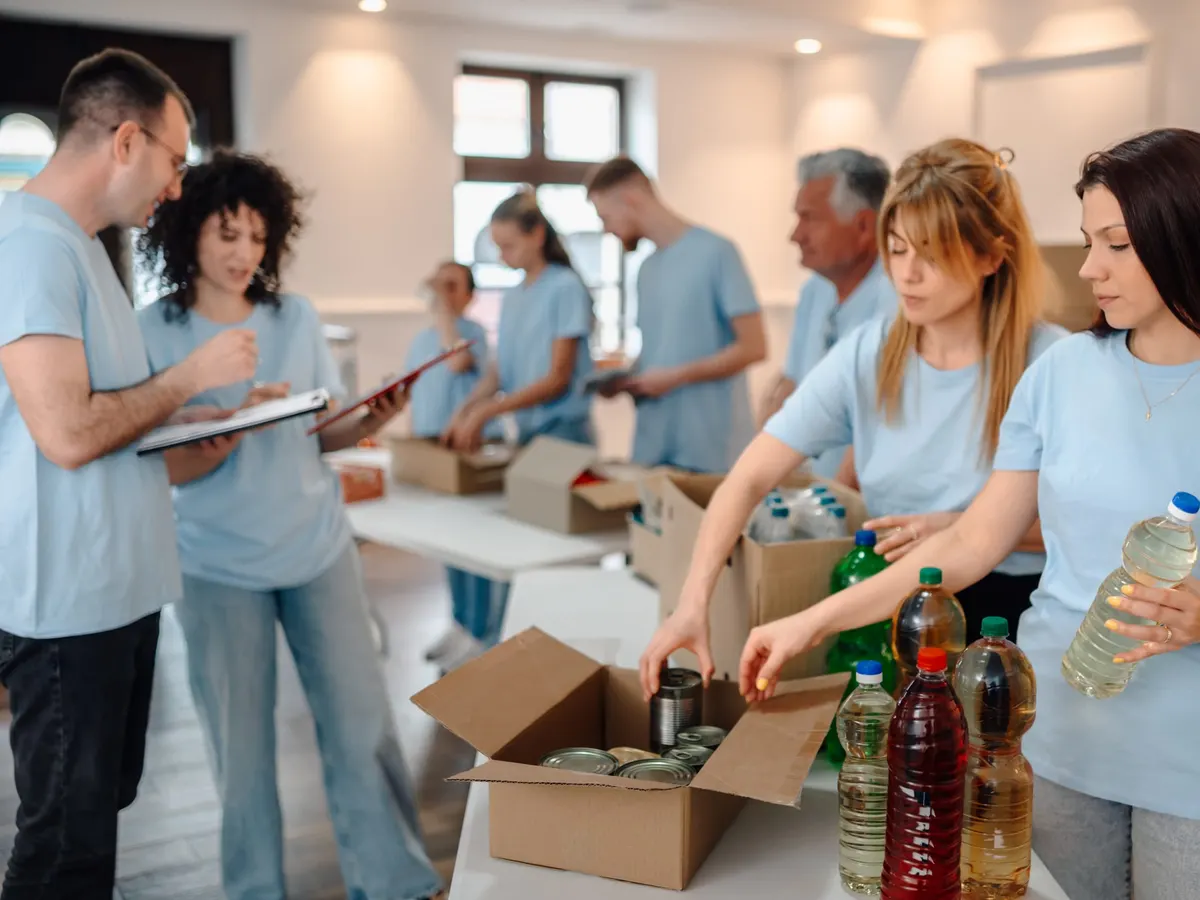 Stock photograph of models: volunteers in matching blue T-shirts sort donated food and drinks into boxes