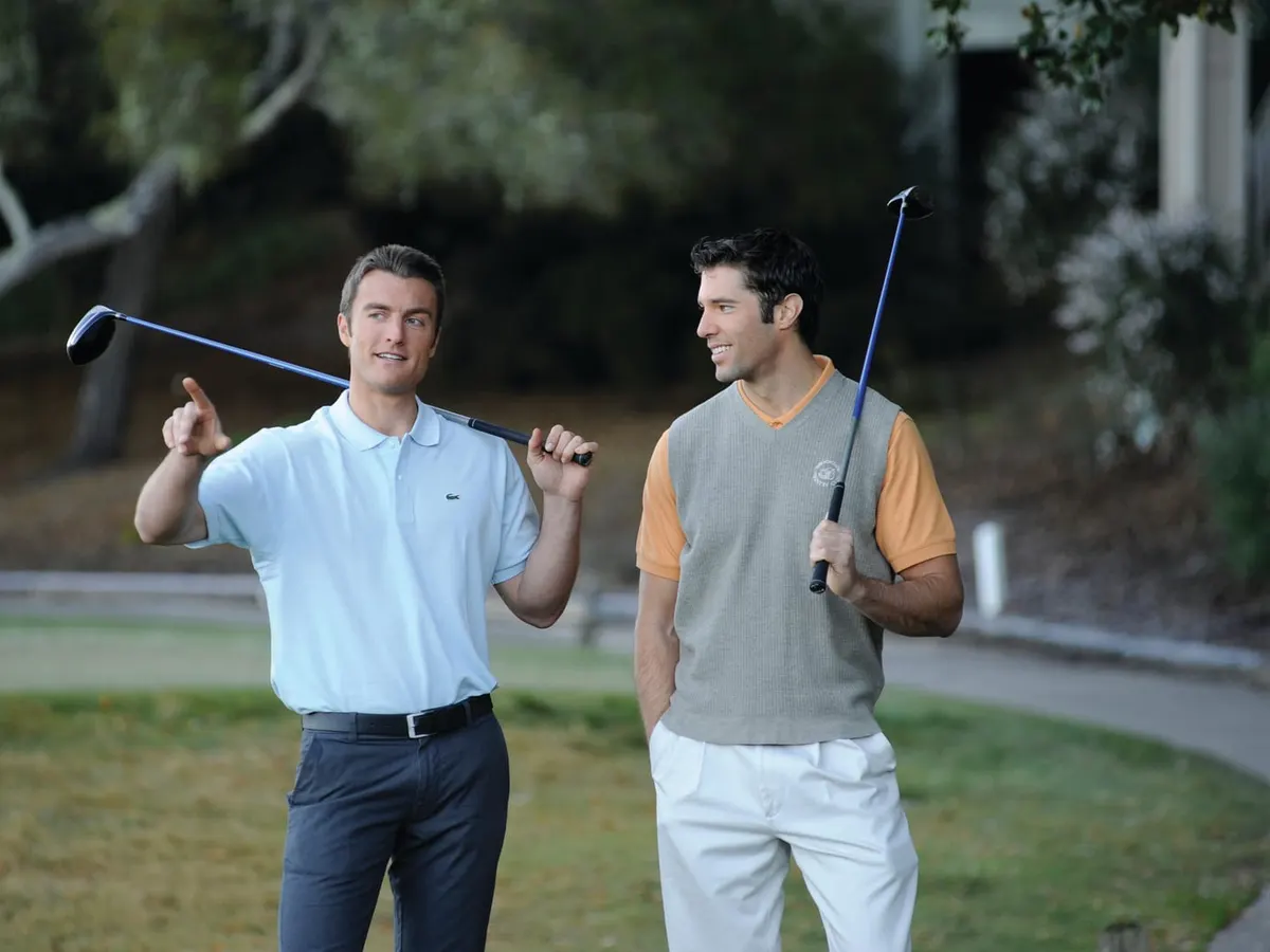 Two men holding golf clubs, talking on a golf course