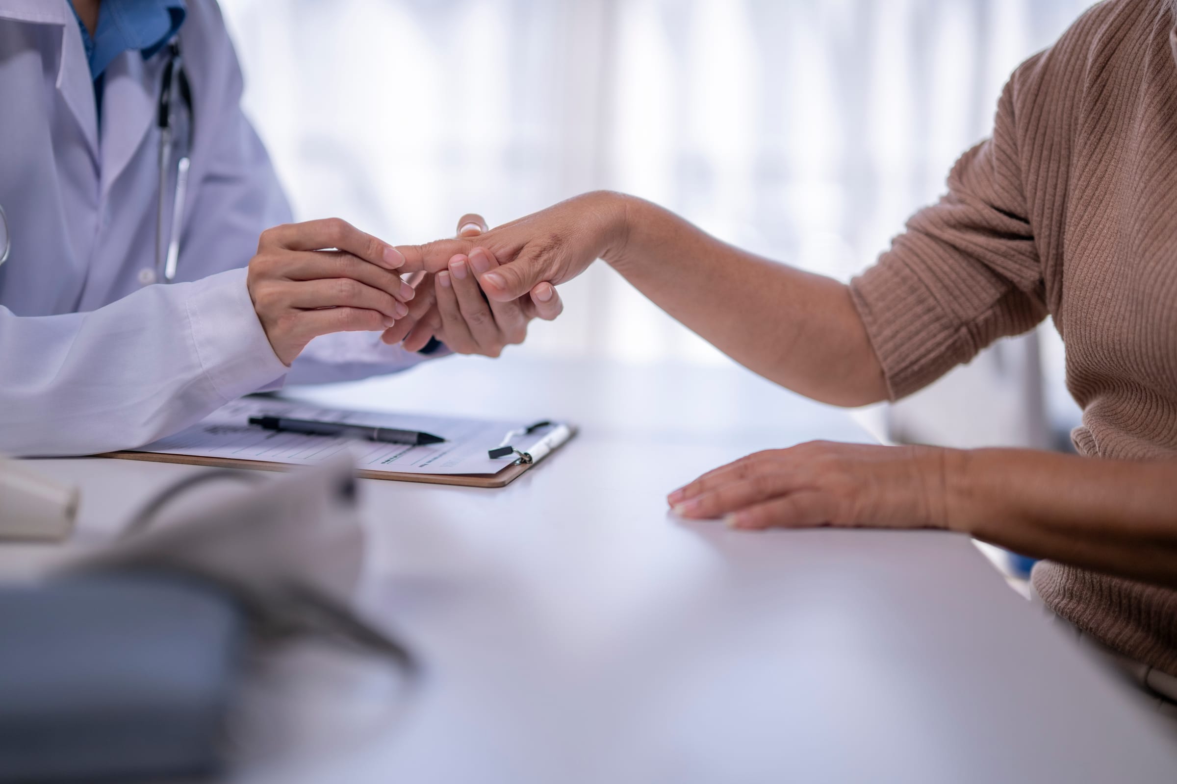 Stock photograph of models: a doctor in a white coat examines a patient’s hand across a desk