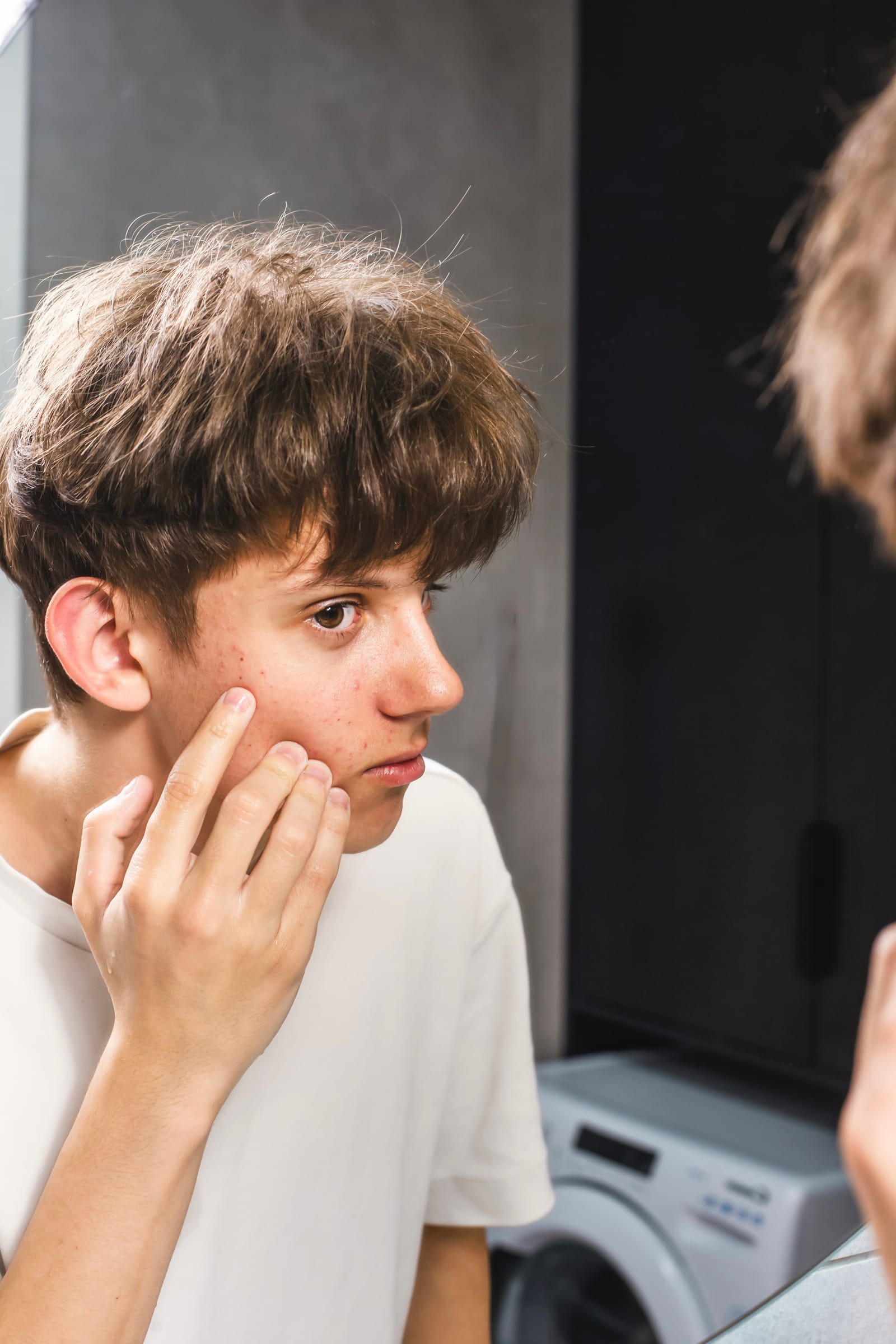 Stock photograph of a model: a teenage boy looks in a mirror and touches a blemish on his cheek