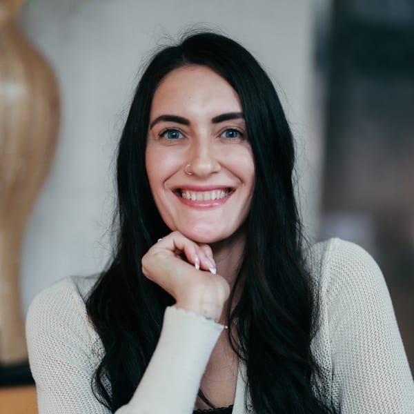 Sara Caddell, smiling, resting her chin on her hand, in a cream sweater