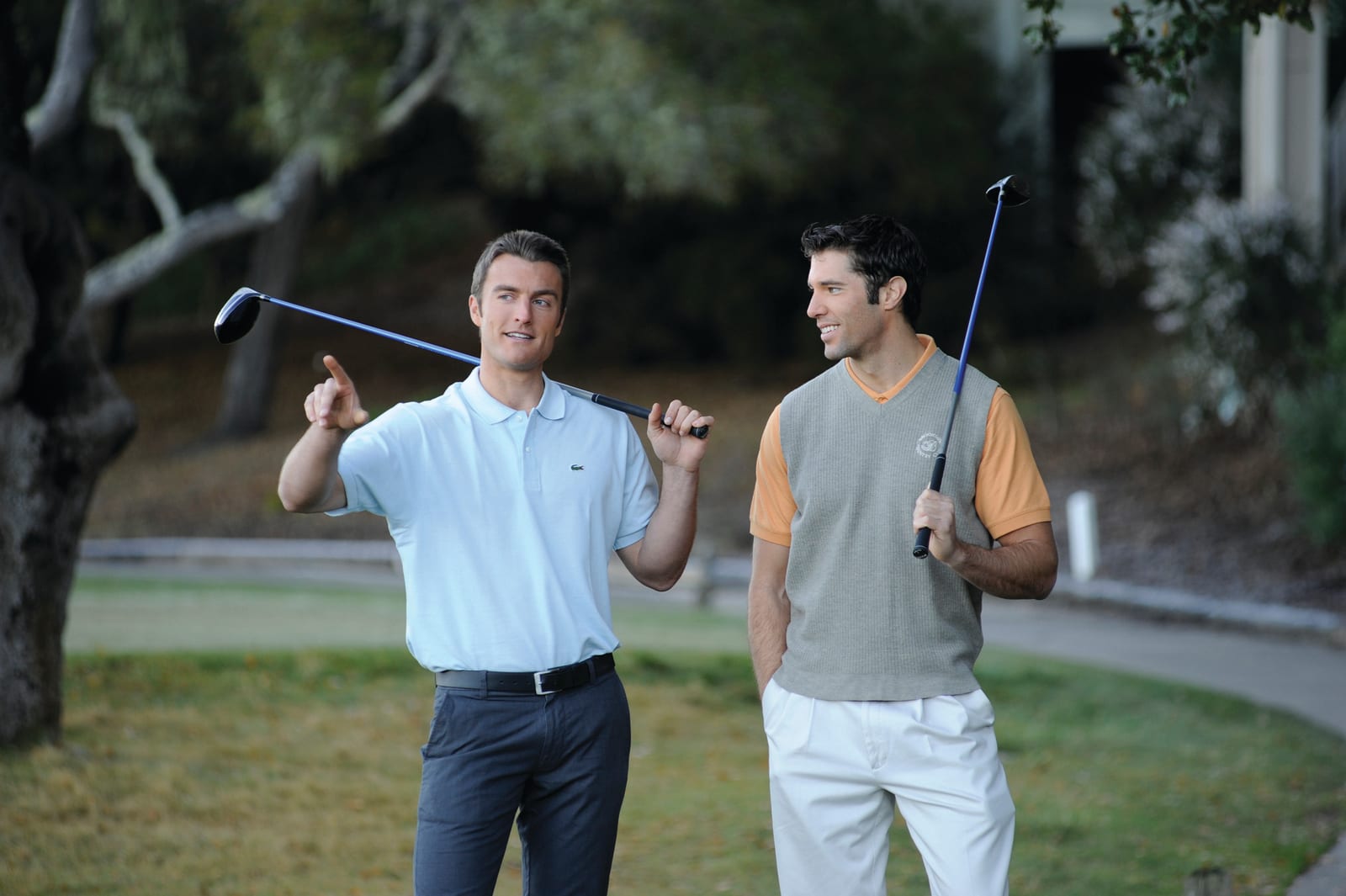 Two men holding golf clubs, talking on a golf course