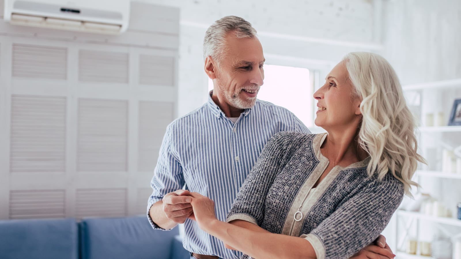 A smiling grey-haired couple dancing together in a bright living room