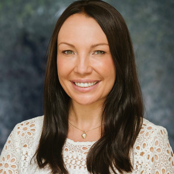 Clisty Taylor, smiling, with long dark hair and a white lace top, against a mottled blue backdrop