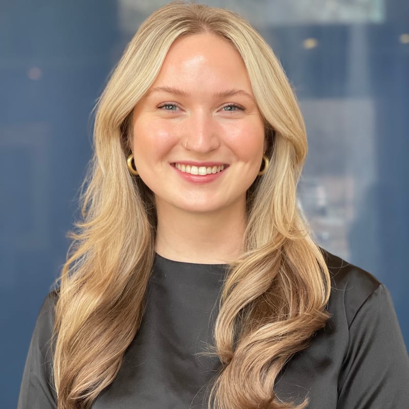 Kalli Duling, smiling, with long blonde hair and a dark top, against a soft blue backdrop