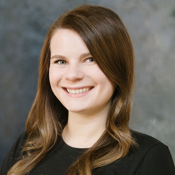 Ashley Williams, smiling, with long brown hair, against a mottled grey backdrop