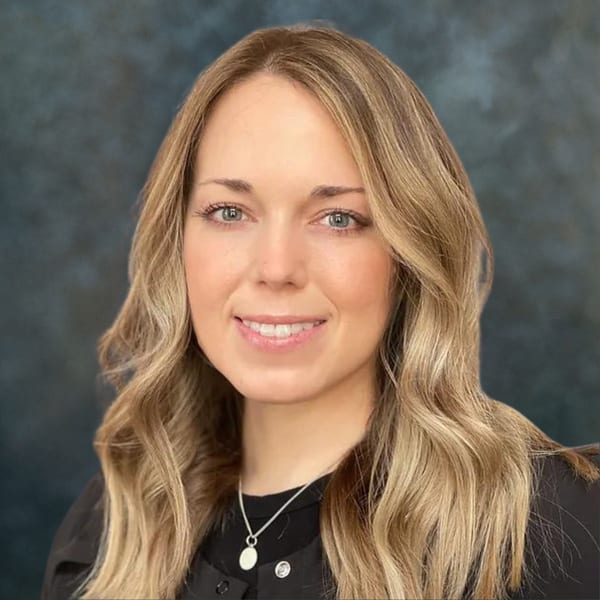 Jackie Fitzgerald, smiling, with wavy blonde hair, against a mottled grey backdrop